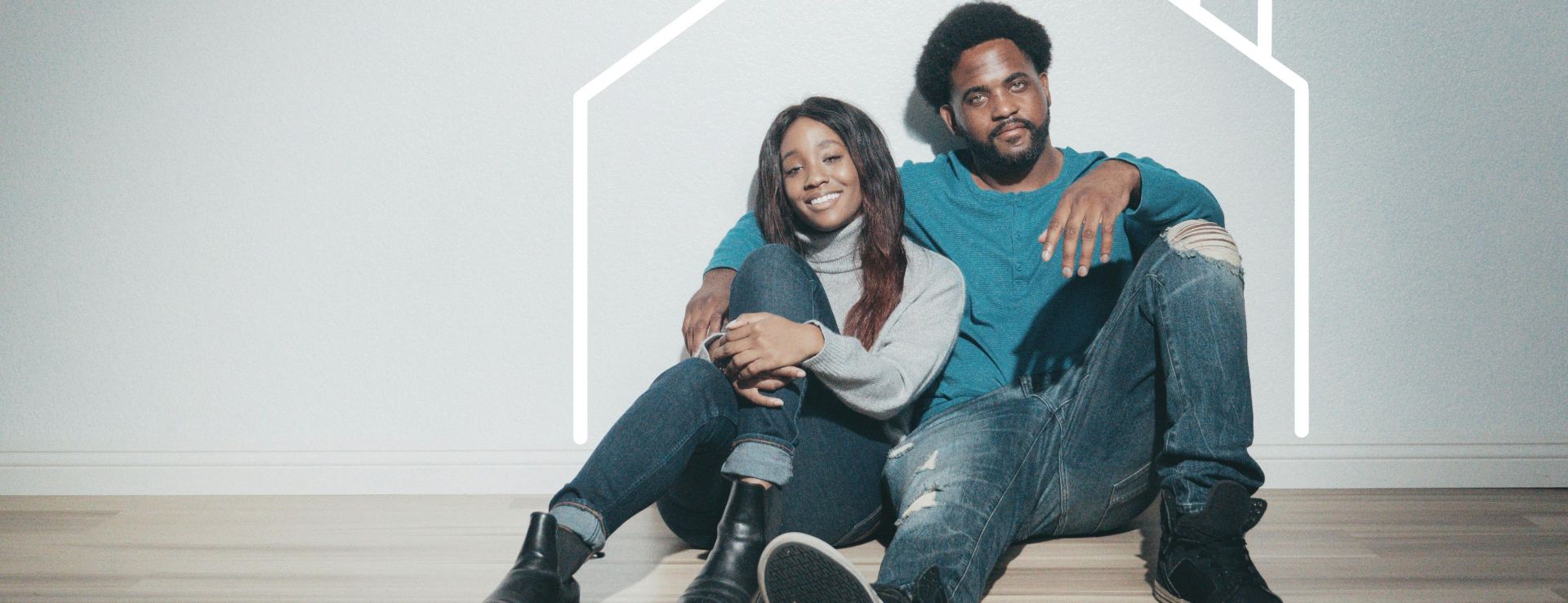 A joyful couple sitting indoors with a house outline, symbolizing their new home.